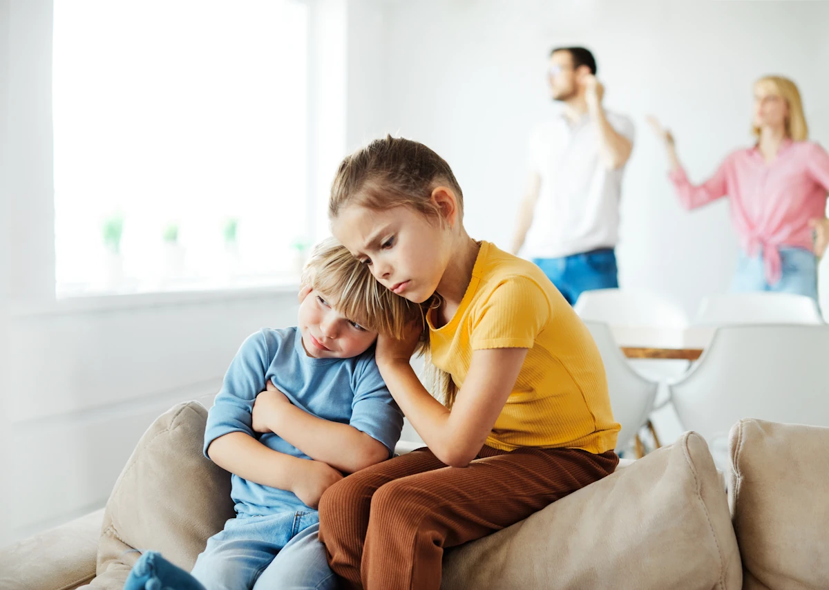 Des enfants assis dans le canapé pendant qu'un couple se dispute à l'arrière